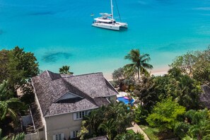 A coastal property with a large house, a beach, and a sailboat in the water.