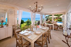 Un comedor amplio con vistas al océano, que cuenta con una gran mesa dispuesta para seis personas, rodeada de sillas de mimbre.