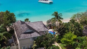 Une propriété située sur la côte, avec une grande maison, une piscine et un voilier visible au loin.