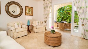 Un salón espacioso con sofás color beige, un otoman de mimbre redondo y un espejo grande.