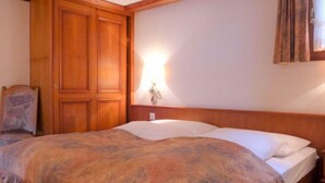 Ein Schlafzimmer mit einem Holfischschrank, einem Bett mit einem gemusterten Bettüberwurf und einer Wandleuchte.