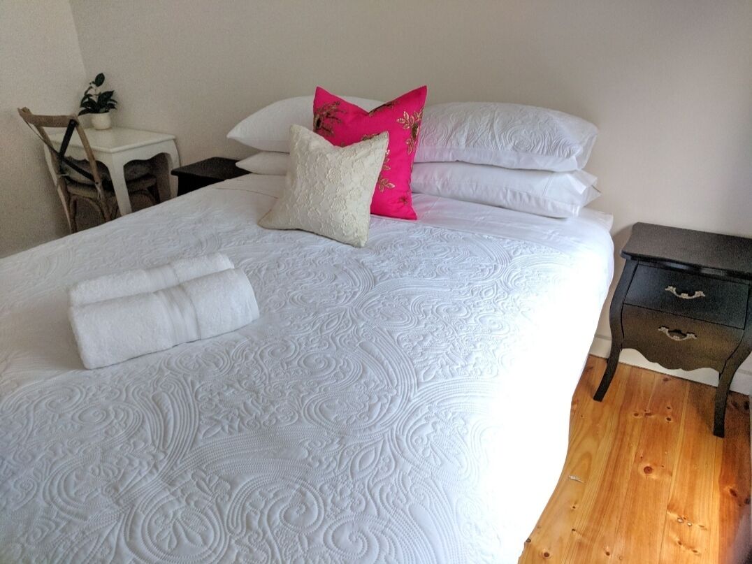 Una cama bien tendida con una colcha estampada, dos almohadas y una toalla blanca doblada.