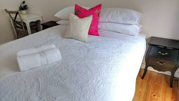 Una cama bien tendida con una colcha estampada, dos almohadas y una toalla blanca doblada.