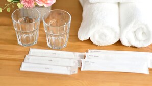 A wooden table with two clear glasses of water, a white towel, and three packets of toothpaste. - Ohma 2312 (Osaka)