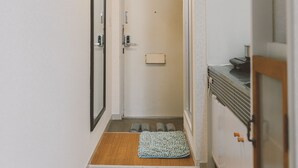 Een smalle gang met houten vloeren, een witte deur en een klein tapijt dat naar een badkamer leidt.
