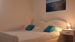 A bedroom with a bed, two pillows, a nightstand with a lamp, and a painting on the wall.