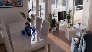 A modern living room with a dining area, large windows, and a painting of sailboats.