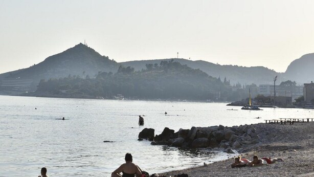 A beach with rocky shore, calm water, and hills in the background.