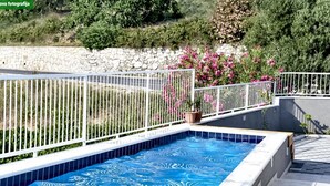 A swimming pool with a white tiled edge, surrounded by a white metal fence, and a stone wall in the background.