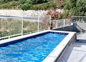 A swimming pool with a white tiled edge, surrounded by a white metal fence, and a stone wall in the background. - Villa Nika - Five-Bedroom Villa with Pool (Mlini)
