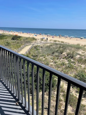 A beach view from a balcony with a railing, sandy beach, and ocean in the background.