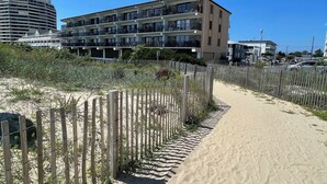 A sandy beach path with a wooden fence, a multi-story building with balconies, and a clear blue sky. - Bimini 205 - Direct Oceanfront 87th St, WiFi, W/D, AC (Ocean City)