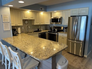 A modern kitchen with granite countertops, stainless steel appliances, and white cabinetry.