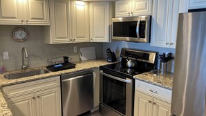 A modern kitchen with white cabinetry, stainless steel appliances, a granite countertop, and a built-in microwave. - Bimini 205 - Direct Oceanfront 87th St, WiFi, W/D, AC (Ocean City)