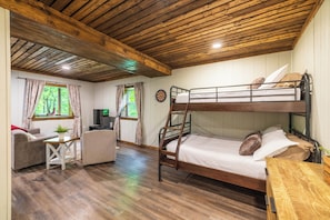 A bunk bed room with a wooden ceiling, a desk, a television, and a window with curtains.