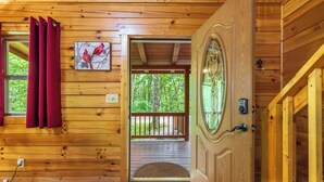 A wooden cabin interior with a door leading to a deck, a red mat at the entrance, and a painting of birds on the wall. - Spacious Log Cabin with Hot Tub, Fire Pit, Large Decks & Wood Fireplace (Logan)