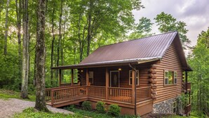 A log cabin with a porch, surrounded by trees. - Spacious Log Cabin with Hot Tub, Fire Pit, Large Decks & Wood Fireplace (Logan)
