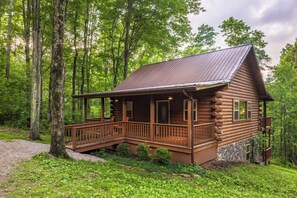 A log cabin with a porch, surrounded by trees.