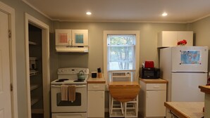 A compact kitchen with white appliances, a window with blinds, and a small dining area.