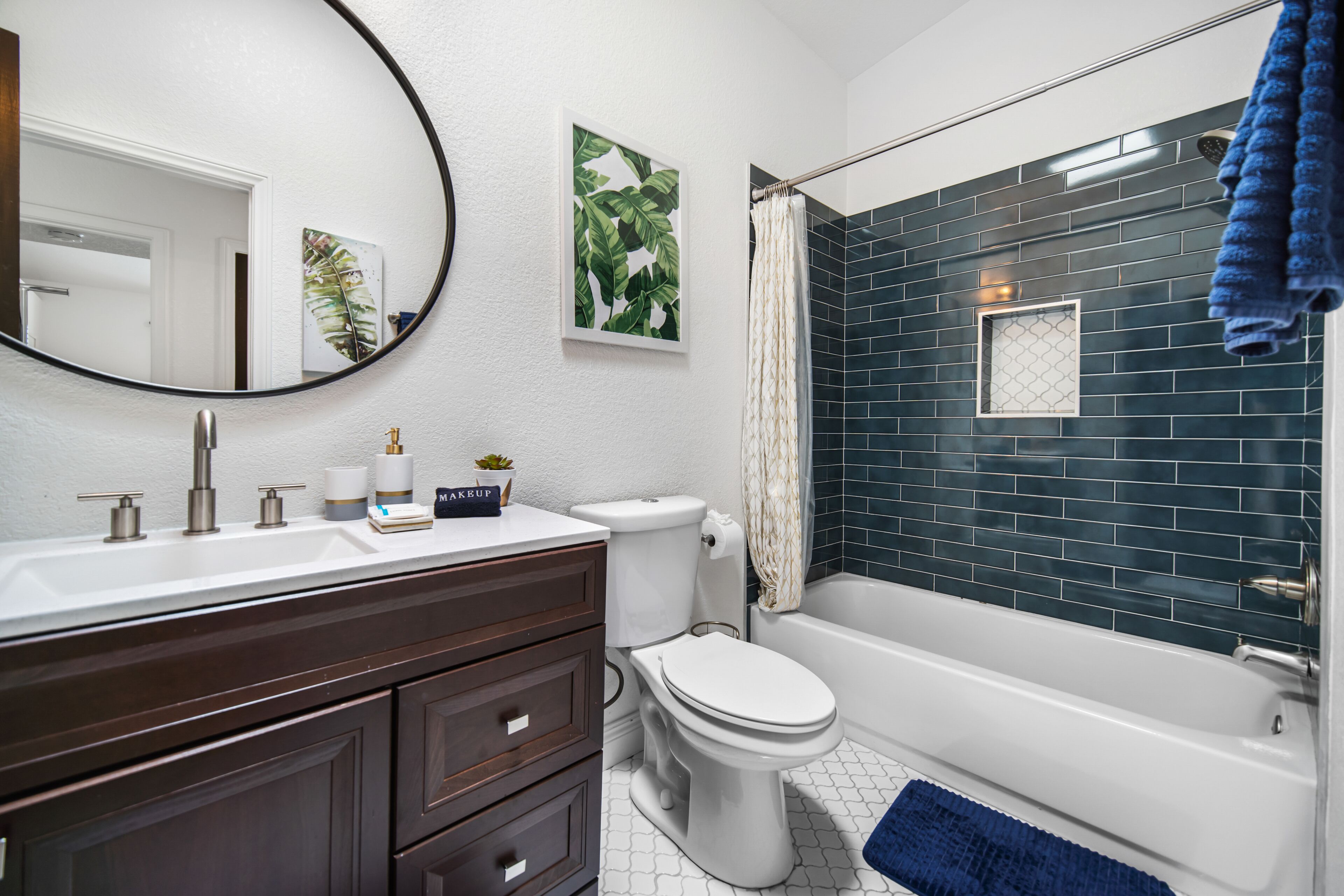 A bathroom with a white sink, dark wooden vanity, a toilet, and a bathtub with dark blue tiles.