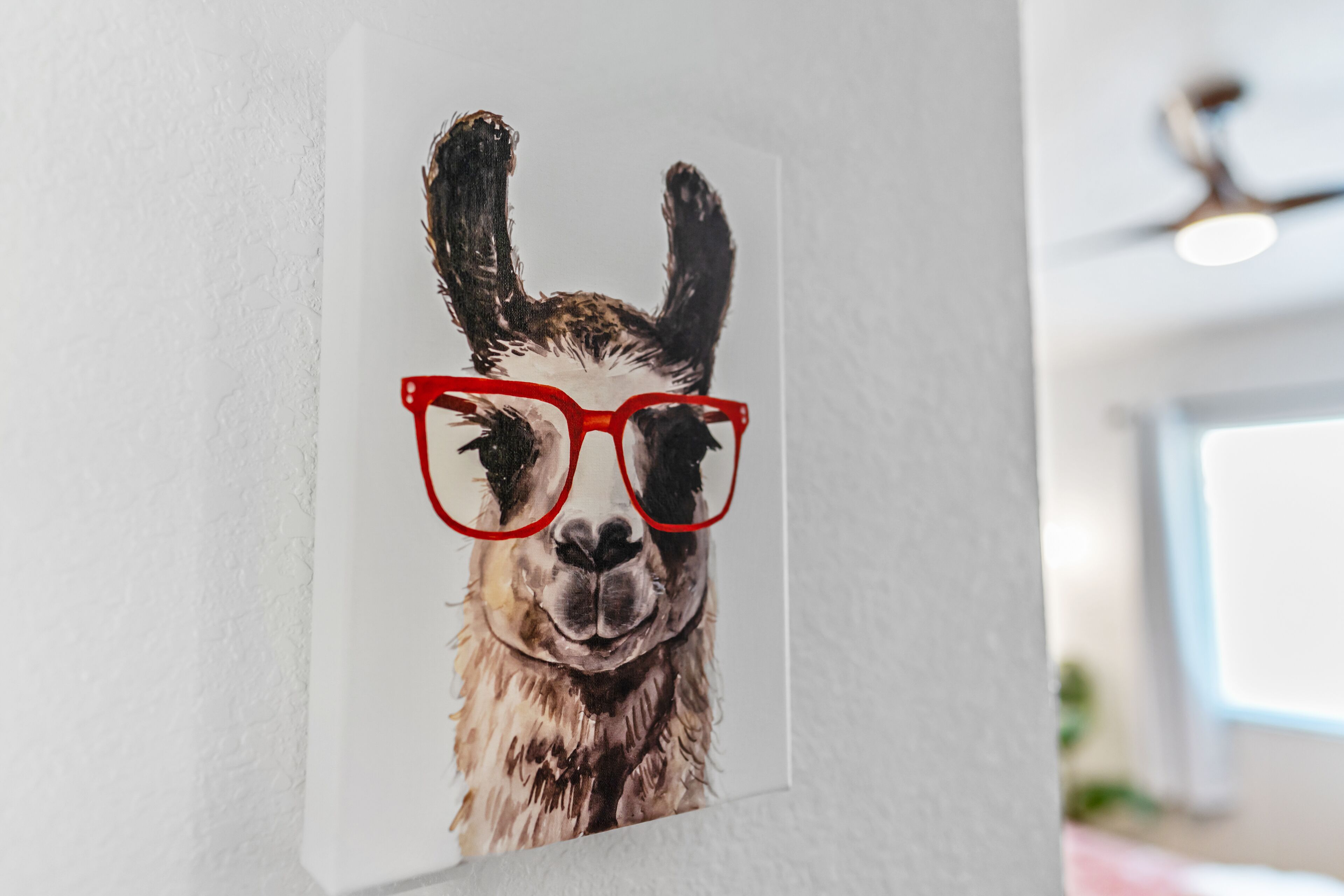 A wall with a framed picture of a llama wearing red glasses.