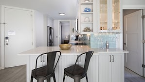 Une cuisine moderne avec des meubles blancs, un îlot central doté de deux chaises et des meubles hauts avec des portes en verre.