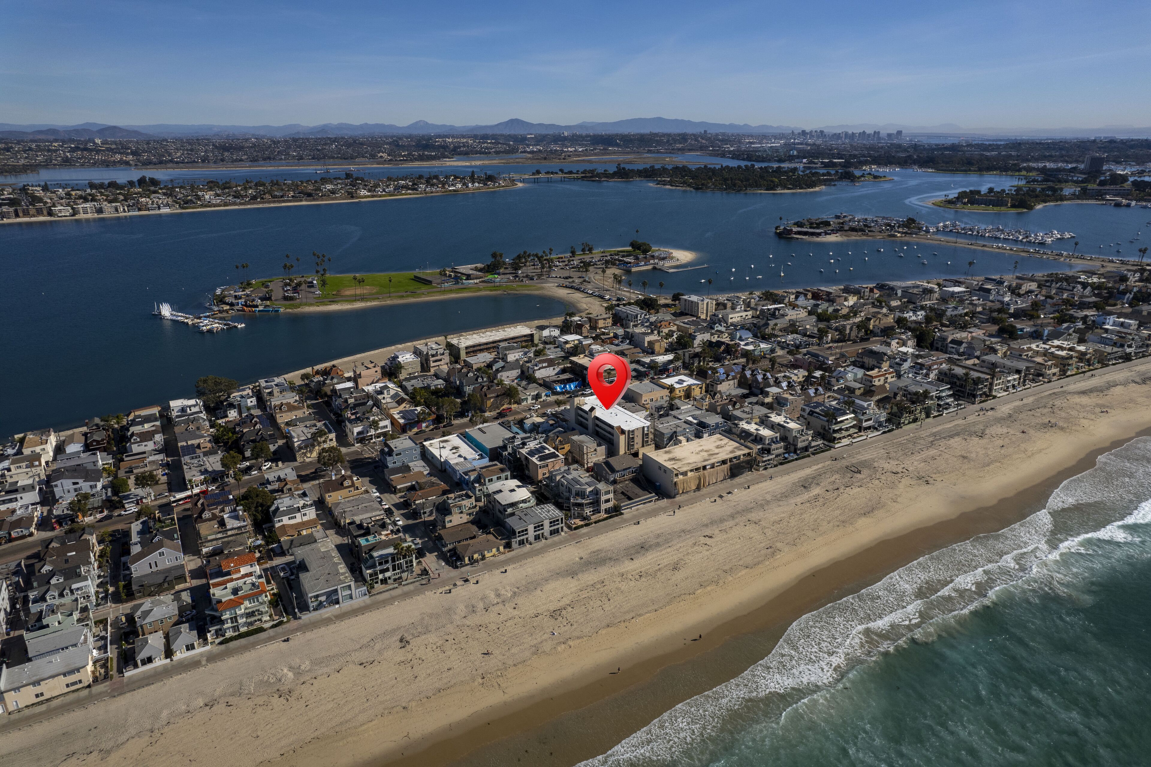 An aerial view of a coastal town with a beach, marina, and residential area.