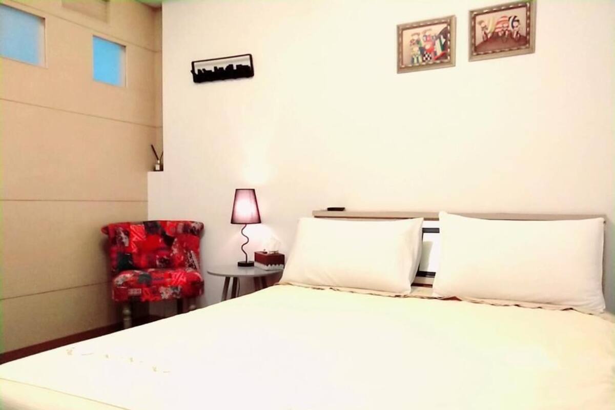 A hotel room with a bed, a chair, a lamp, and two framed pictures on the wall.