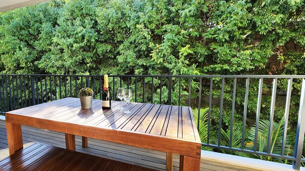 A wooden deck with a table and chairs, surrounded by a black metal railing, overlooking a lush green garden. - Stylish Parkside Retreat - Outdoor Pool & Undercover Parking - Randwick (Randwick)