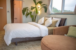 A bedroom with a bed, a sofa, a potted plant, and a window.