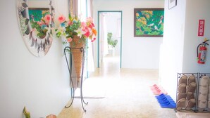 A hallway with a wicker plant stand, a fire extinguisher, and a shoe rack. - Coco Calm (Uruma)