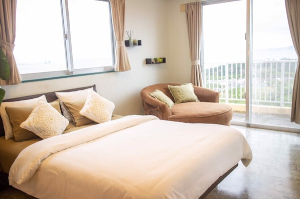 A hotel room with two beds, a sofa, and a balcony with a view.