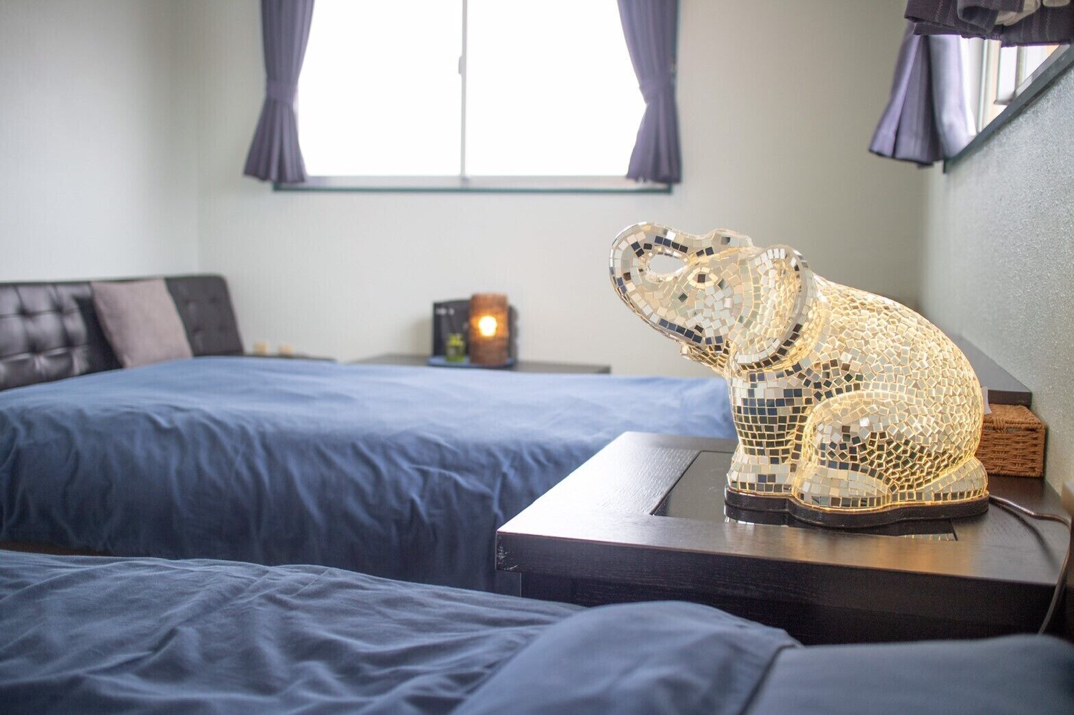 A room with two beds, a nightstand with a lamp, and a decorative mosaic sculpture on a table.