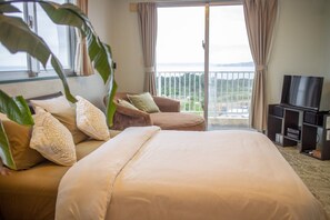 A hotel room with a large bed, a sofa, a TV, and a balcony with a view of the sea. - Coco Calm (Uruma)