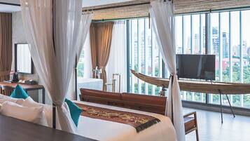 A modern hotel room with a large bed, a desk, a TV, and a view of the city through large windows.