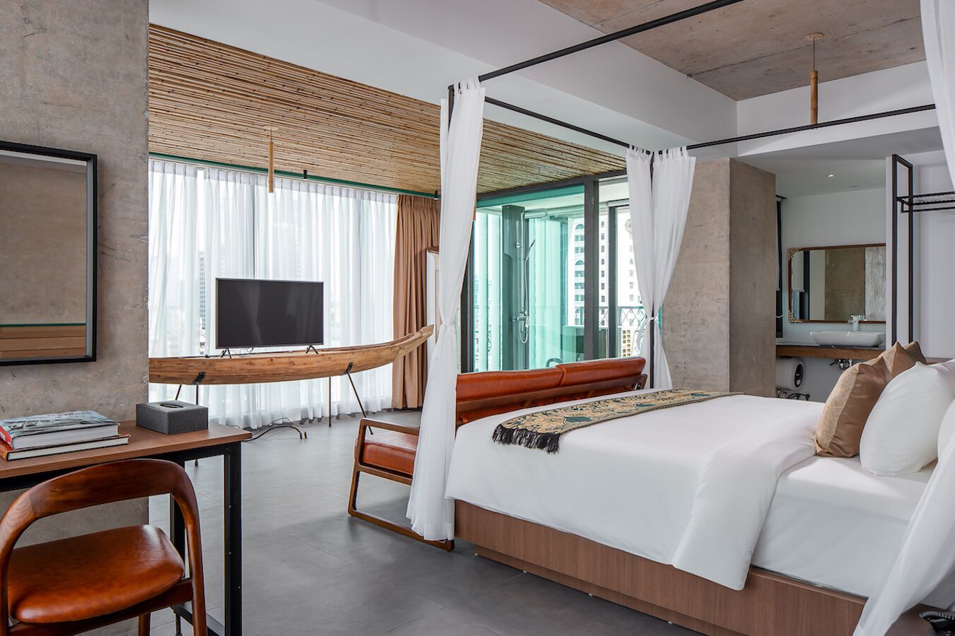 Una habitación de hotel moderna con una cama grande, un escritorio con televisor y vistas a la ciudad a través de amplios ventanales.