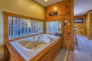 Una cabaña de madera con una bañera de madera grande, un letrero que dice 'Welcome' y una vista a través de un ventanal decorativo.