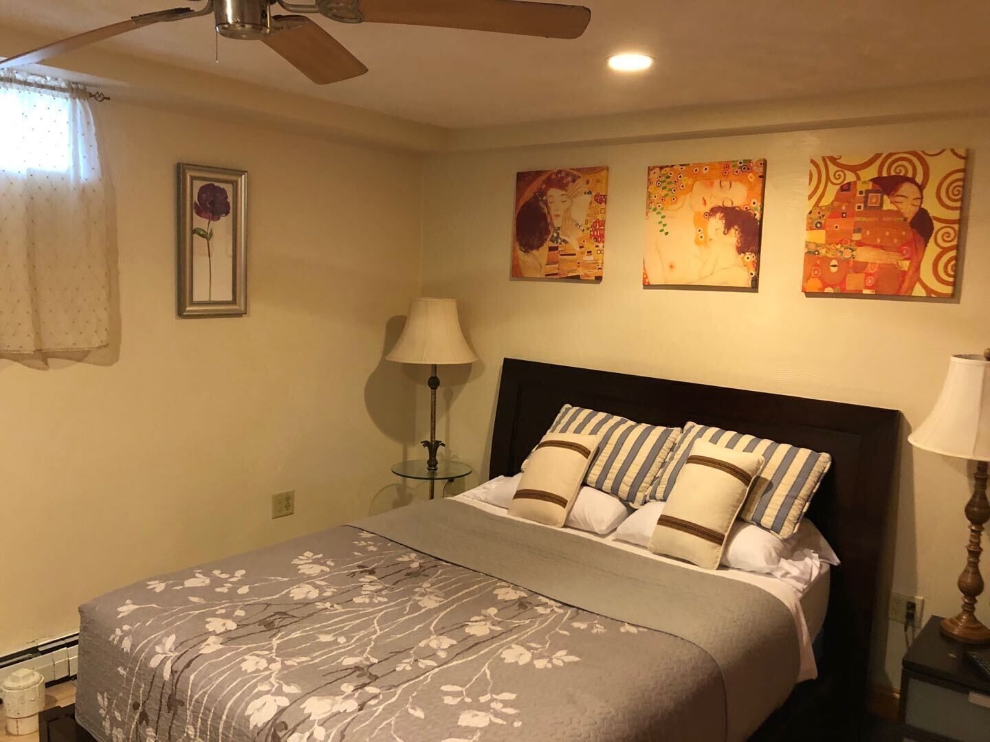 Quarto com cama, ventilador de teto, luminária de chão e três quadros na parede.