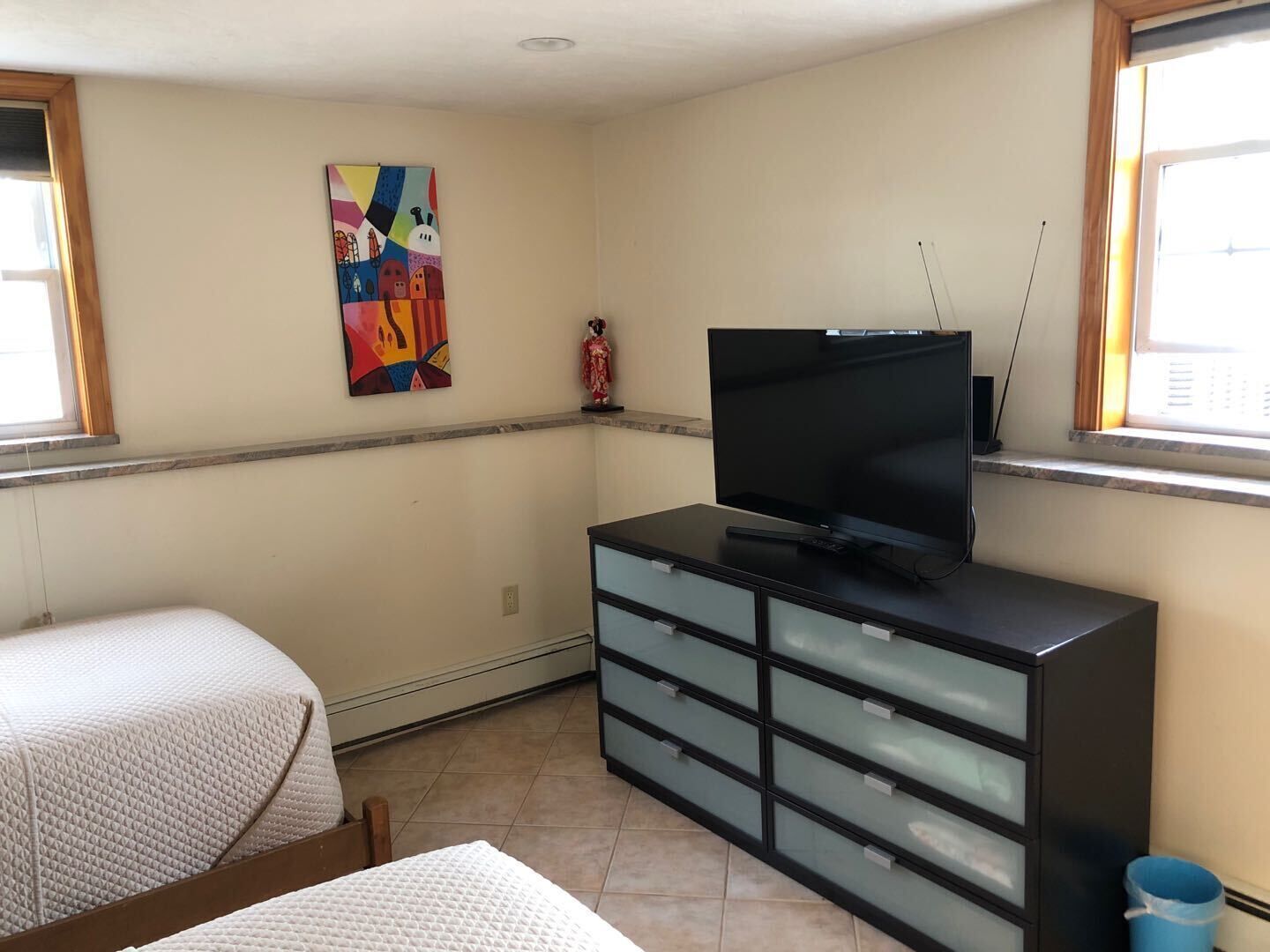 A bedroom with a bed, a dresser, a television, and a painting on the wall.