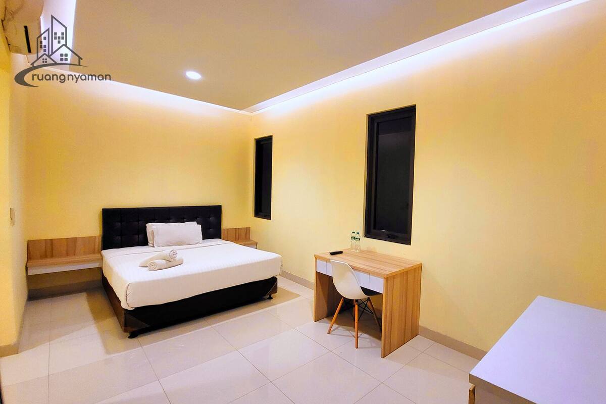 A hotel room with a bed, a desk, a chair, and a TV.