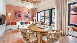 A spacious living room with a round wooden table, wicker chairs, a beige sofa, and artwork on the walls.