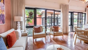 A spacious living area with a sofa, armchairs, a dining table, and a view of a tropical garden through large windows.
