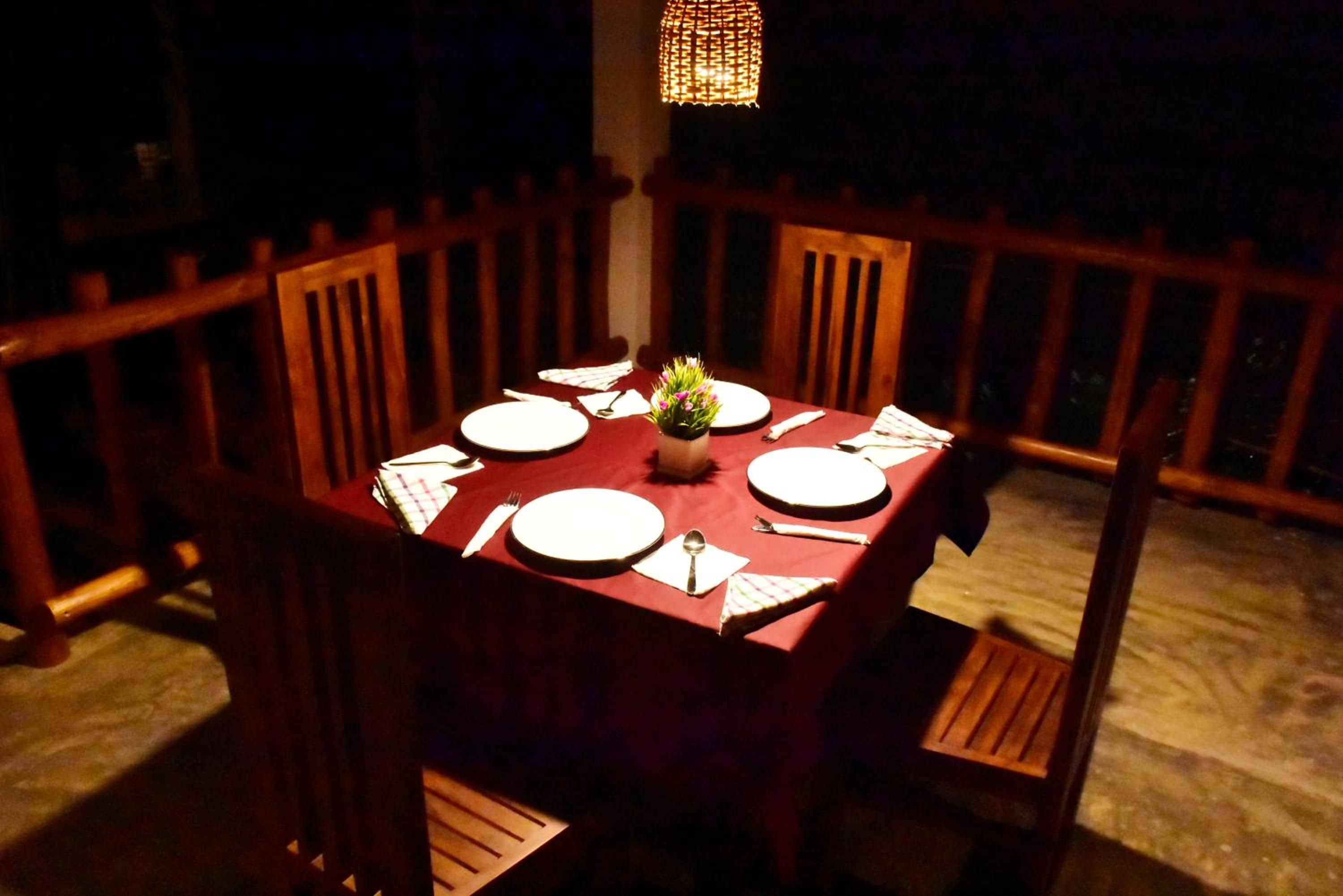 A dining table set for four with a red tablecloth, surrounded by wooden chairs, and a hanging light fixture above.