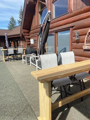 Un espace extérieur aménagé avec des tables et des chaises en bois, un parasol et une vue sur un chalet en bois.