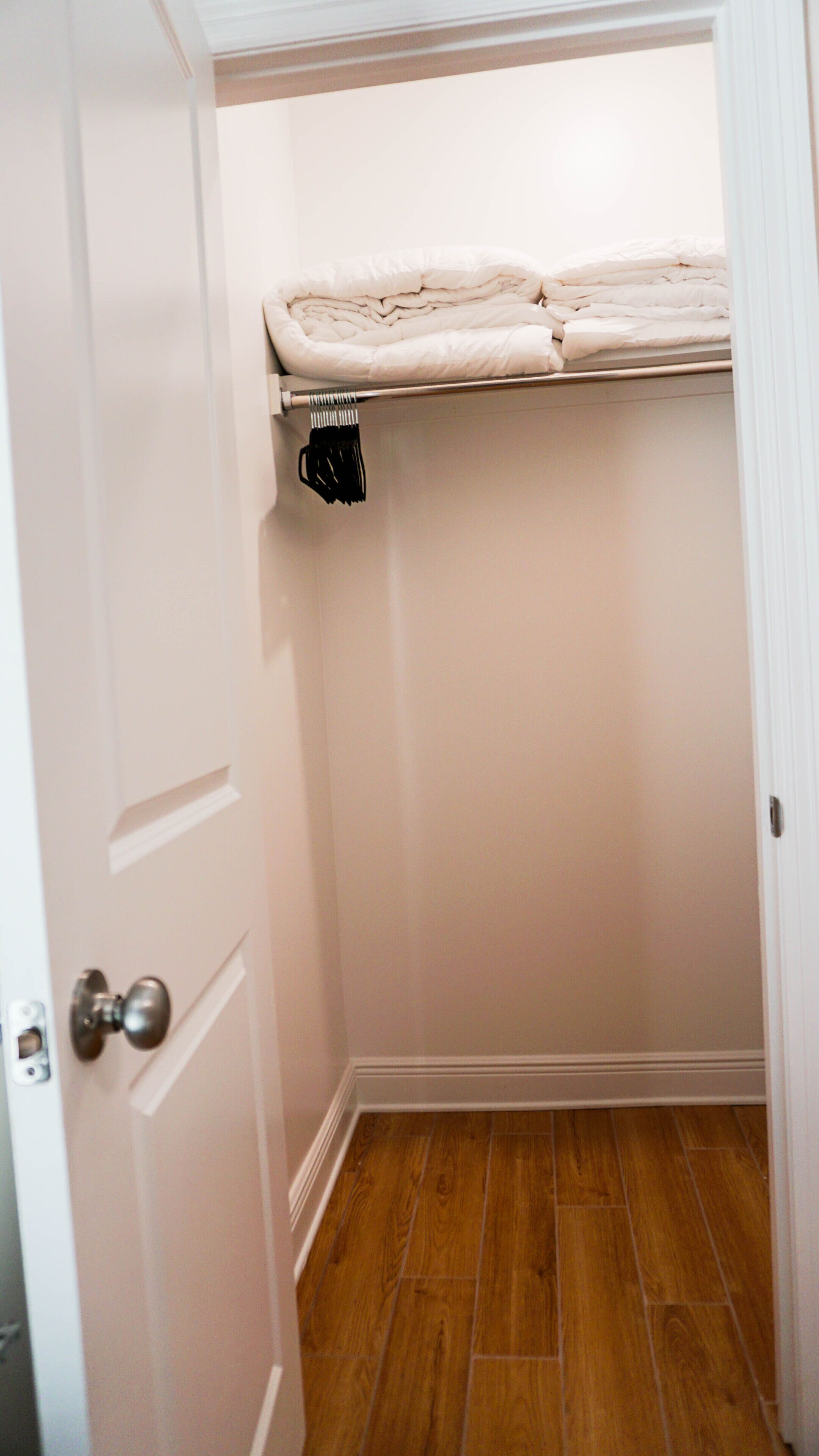 A small closet with a wooden floor, a white door, and a shelf above the door.