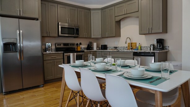 A modern kitchen with grey cabinets, stainless steel appliances, and a dining area set for four. - 🔥WALK 2 BEACH❤️ | SLEEPS 6 W/ W+D (Biloxi)