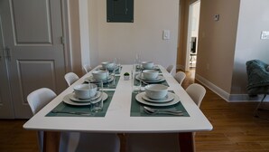 A dining table set for six with white plates, bowls, and clear glasses, surrounded by white chairs. - 🔥WALK 2 BEACH❤️ | SLEEPS 6 W/ W+D (Biloxi)