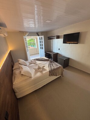 A bedroom with a bed, a desk, a chair, a TV, and a door leading to a balcony. - Hotel Pousada Villa Marina (Fortaleza)