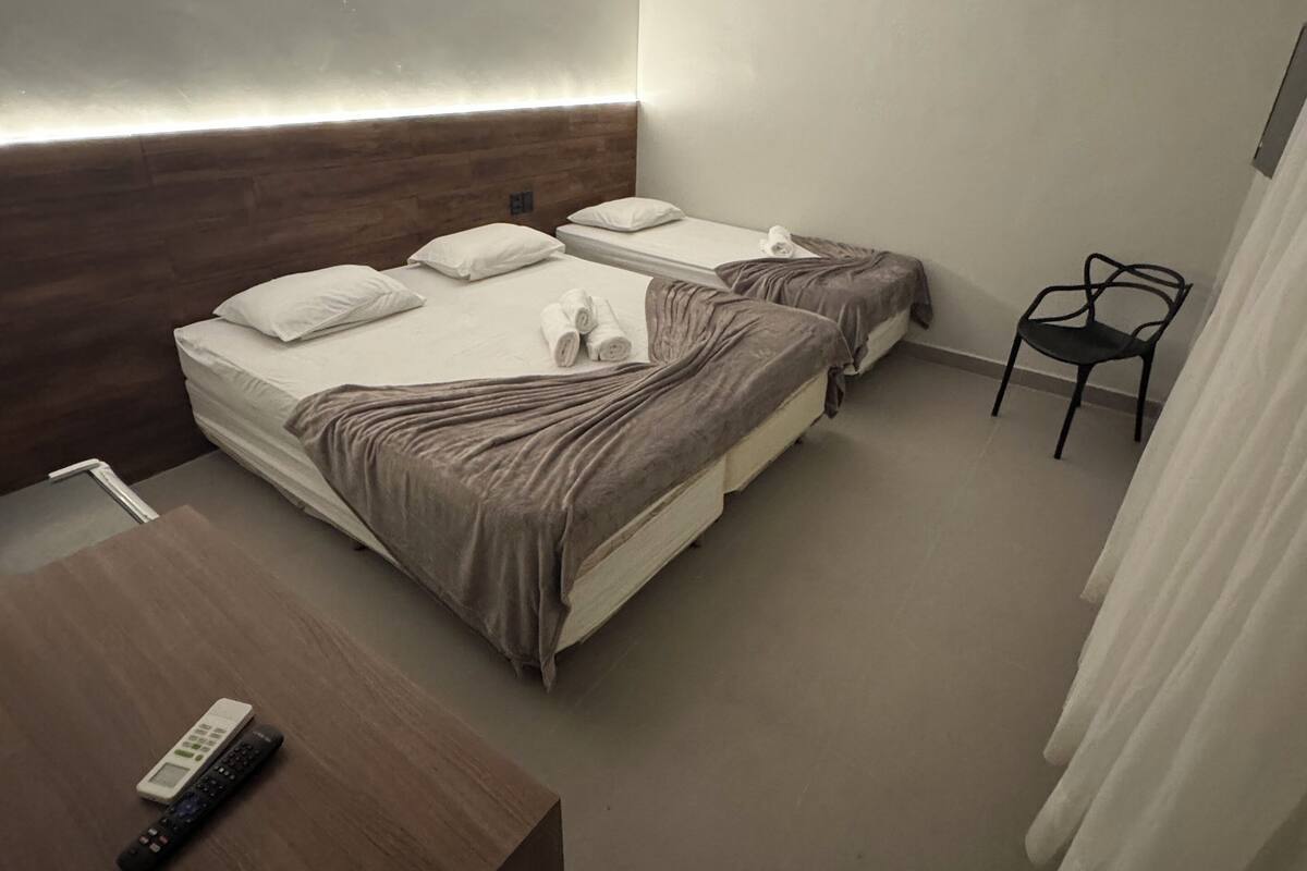 Ein Hotelzimmer mit zwei Betten, einem Holztisch, einem Stuhl und einer Klimaanlage.