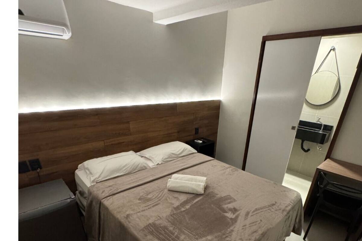 Ein modernes Hotelzimmer mit einem Holzkopfteil, einem Nachttisch, einer kleinen Nachttischlampe und einem Spiegel an der Wand.